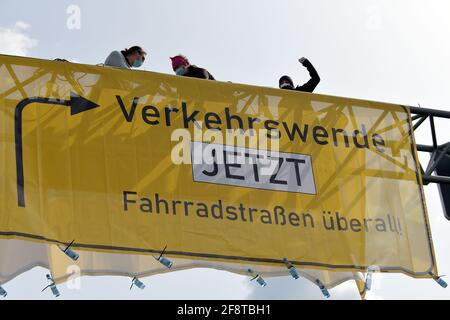Bremen, Germany. 15th Apr, 2021. Activists of the organization 'Extinction Rebellion' sit above a banner hanging over a motorway feeder road in Bremen. By occupying the truss above the roadway, the activists want to draw attention to their concerns in the course of the conference of transport ministers hosted in Bremen. Credit: Michael Bahlo/dpa/Alamy Live News Stock Photo
