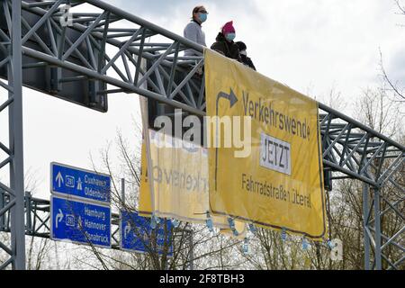 Bremen, Germany. 15th Apr, 2021. Activists of the organization 'Extinction Rebellion' sit above a banner hanging over a motorway feeder road in Bremen. By occupying the truss above the roadway, the activists want to draw attention to their concerns in the course of the conference of transport ministers hosted in Bremen. Credit: Michael Bahlo/dpa/Alamy Live News Stock Photo