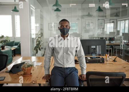 African businessman in a mask leaning on an office desk Stock Photo