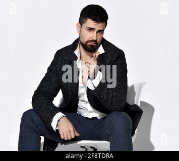 Young stylish bearded man in jeans and casual tweed jacket is sits on chair gesturing pointing with finger at camera Stock Photo
