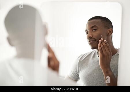 African man applying lotion on his face in his bathroom mirror Stock Photo