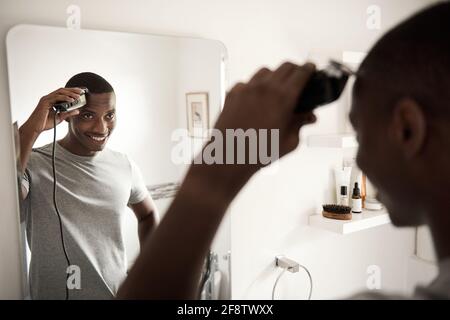 Smiling African man trimming his hair in his bathroom mirror Stock Photo