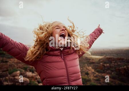 Close-up of a beautiful woman on mountain trail with her hair flying and hands outstretched with mouth open