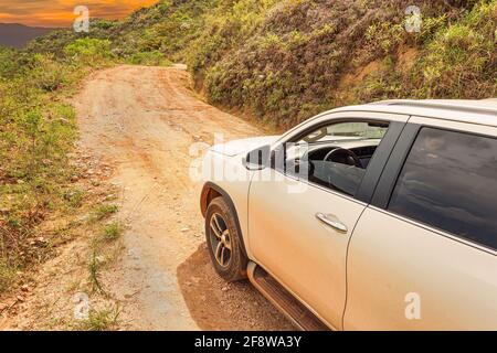 SUV car going up the sierra on a rocky road, white car on sloping ground during sunset.  Concept of eco tourism 4x4 adventure. Brazilian sierra of the Stock Photo