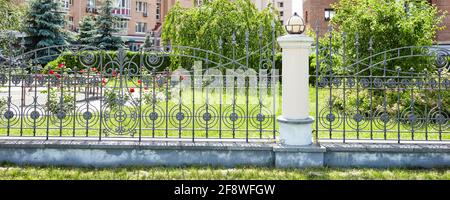 Wrought iron fence. Image of a Beautiful decorative cast iron wrought fence with artistic forging and stone columns Stock Photo