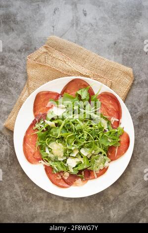 Italian typical dish called 'carpaccio' of breasaola meat (from cow) and aragula and parmesan cheese Stock Photo