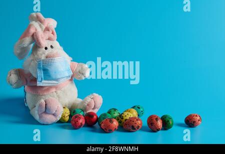 on a blue background white hare in a mask and Easter eggs Stock Photo