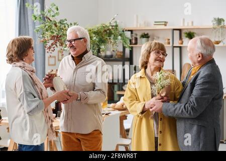 Group of senior friends meeting with each other they giving presents and talking while standing in the room Stock Photo
