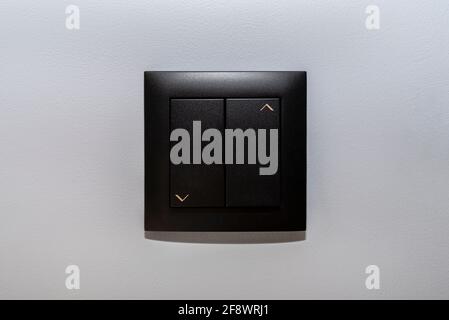 Black frame and button of the roller shutter switch up and down on gray wall in the house. Stock Photo