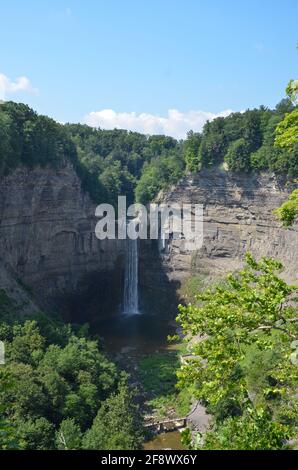Breathtaking waterfall named Taughannock Falls that falls from a forest river over a huge rock face into a valley lake in sunny weather Stock Photo