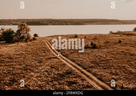 couple in love man and woman are walking along vast deserted meadow on grass in summer hot warm weather at sunset in nature. sun over river. top aeria Stock Photo