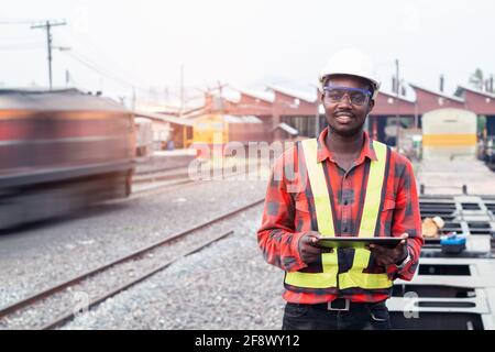African man engineer using tablet to report of Train Timetables for control a the train on railway Stock Photo