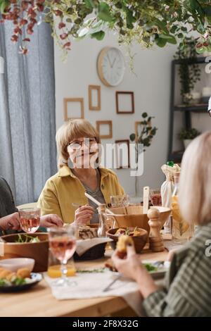 Happy senior woman sitting at dining table and having dinner with her friends at home Stock Photo
