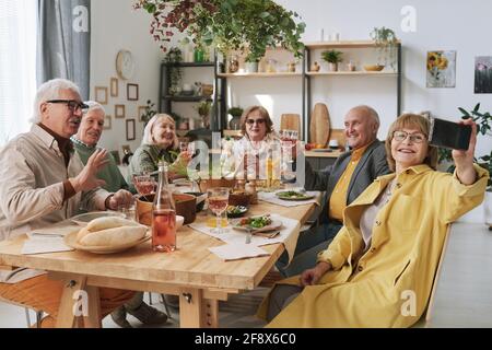 Senior woman making selfie with her old friends on mobile phone while they sitting at the table during dinner Stock Photo