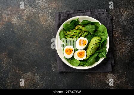 Fresh vegetable salad with avocado, asparagus, crumpled eggs with black sesame seeds and spinach on plate on light slate, stone or concrete background Stock Photo
