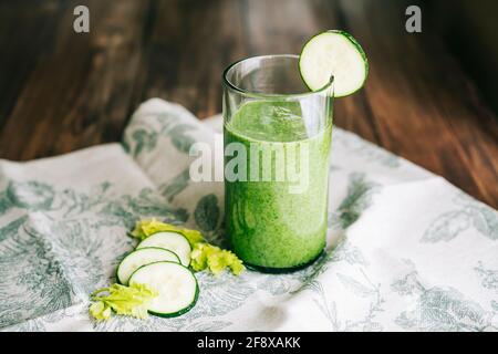 Green smoothie with celery and cucumber in crystal glass on a grey cloth of green leaves on a dark wooden table Stock Photo