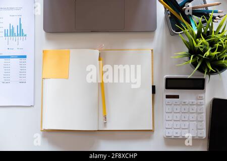 Top view open notebook, pencil, calculator and plant potted on white desk background, Accounting workplace concept Stock Photo