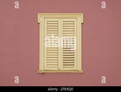 Window wooden shutters on brown color painted wall background. Yellow pale french style closed window blinds with ornamental frame on residential buil Stock Photo