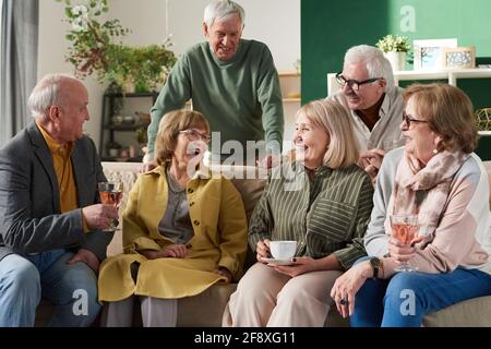 Happy old friends sitting on sofa and talking to each other during meeting in domestic room Stock Photo