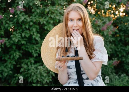 A young woman eats fresh berries on a background of greenery in the park. Stock Photo