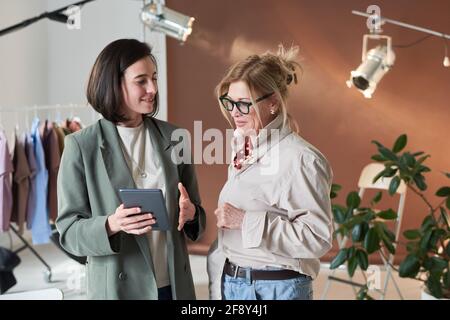 Two fashion designers discussing new collection and using digital tablet while standing at studio Stock Photo