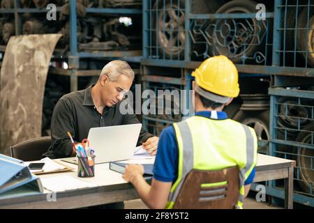 Factory manager looking at the paper with young engineer sitting front for call for blaming or consider and interview job apply or solving working pro Stock Photo