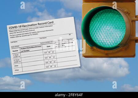 photo collage of covid-19 vaccination record card and a green traffic light against a sky, representing opening as more people are vaccinated Stock Photo