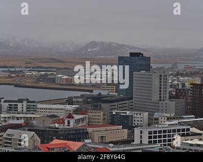 Aerial view over northern part of Reykjavik downtown with buildings, including Fosshotel, and snow-covered mountains on cloudy winter day. Stock Photo