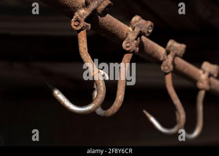 Rusty meat hooks hang from the ceiling against a dark background Stock Photo