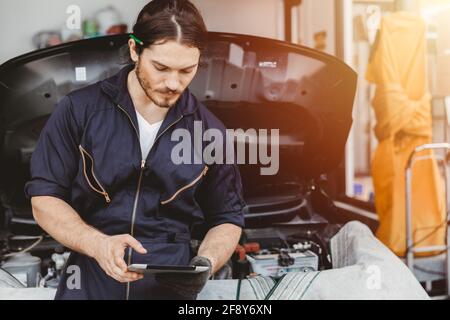 Garage technician worker using tablet computer advance technology for service checking and tuning car ECU at automobile car service center Stock Photo