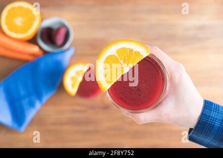 Beet juice in hand with orange decoration on wooden background. Copy space. Top view. Stock Photo