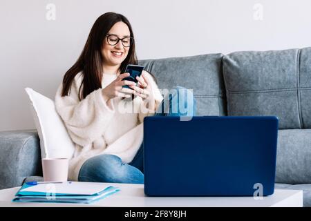 woman talking with mobile phone while working with laptop sitting on a couch at home Stock Photo