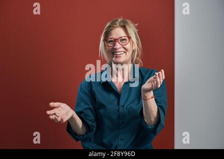 Portrait of happy senior woman in blue blouse standing and laughing against the red background Stock Photo