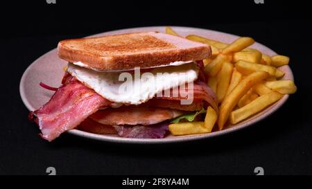 Top view of a double club sandwich with french fries on a plate isolated on black background Stock Photo