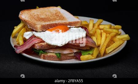 Top view of a doubl club sandwich with french fries on a plate isolated on black background Stock Photo