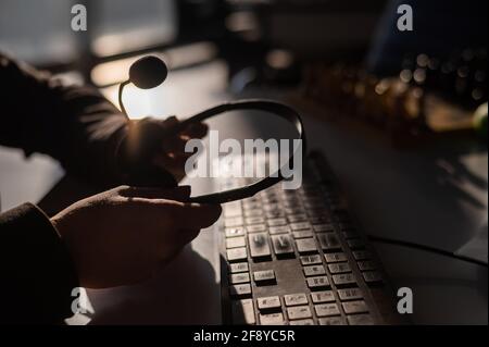 A woman is holding a headset with a microphone over a computer keyboard. Call center operator's workplace Stock Photo