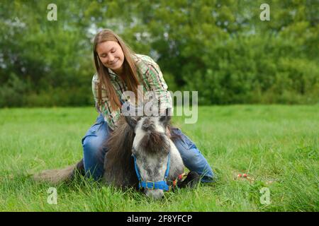 Happy Caucasian woman is training her pony in outdoors. Stock Photo