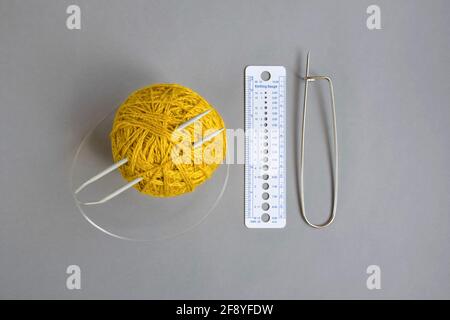 One skein of yellow wool yarn, knitting spokes, measuring ruler and large pin on gray background, handmade, knitting. Close-up. Copy space. Stock Photo