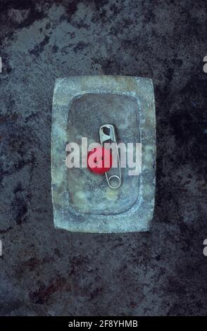 Silver safety pin lying in small grey marble dish with single bright red button Stock Photo