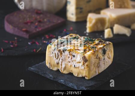 Square piece of soft cheese with colored edible flower petals on a slate plate Stock Photo