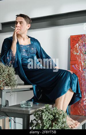 Transsexual in female clothes sitting on stairs thinking about something and smoking a cigarette Stock Photo