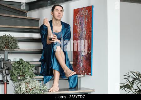 Transgender in female dressing gown smoking a cigarette and drinking a red wine while sitting on stairs Stock Photo