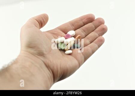 The man holds in his hand pills, vitamins, medicines on a white background. Outstretched hand with handful of pills. Stock Photo