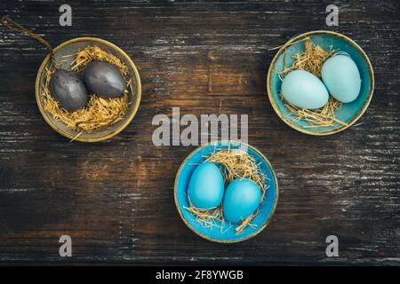 Three small colorful bowls filled with Easter eggs in the same color on rustic wood, Easter decoration, shabby style, top view with copy space Stock Photo
