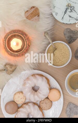 Scene of a cozy coffee break with macarons, donuts, and candle light on lambskin on the wooden floor, natural colors, top view Stock Photo