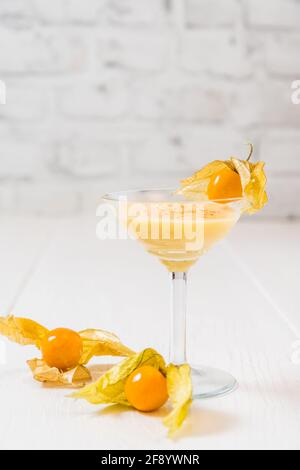 Glass with eggnogg and physalis fruits on white background, vertical with copy space Stock Photo