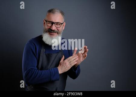 Handsome mature man wearing eyeglasses over gray background clapping and applauding happy and joyful, smiling proud hands together Stock Photo