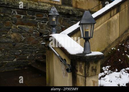 old stone stairs with metal handrail and metal lanterns next to a stone wall with big old stones covered with snow in winter Stock Photo