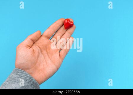 Young man hand gives a small red heart, help and donate concept background photo Stock Photo