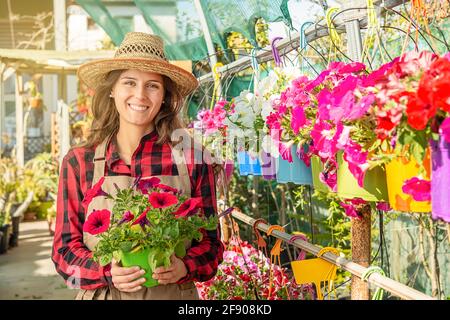 Happy young female smiling florist working in a greenhouse in garden center with red flowers Stock Photo